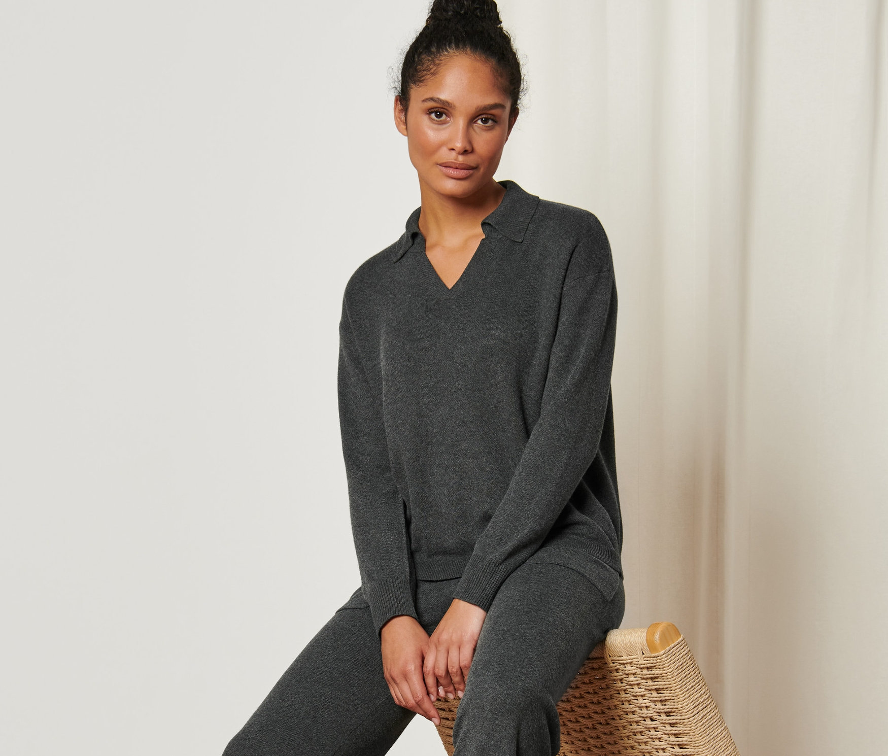 Frau sitzt auf einem Rattanstuhl und trägt einen Strickpullover mit Polokragen.