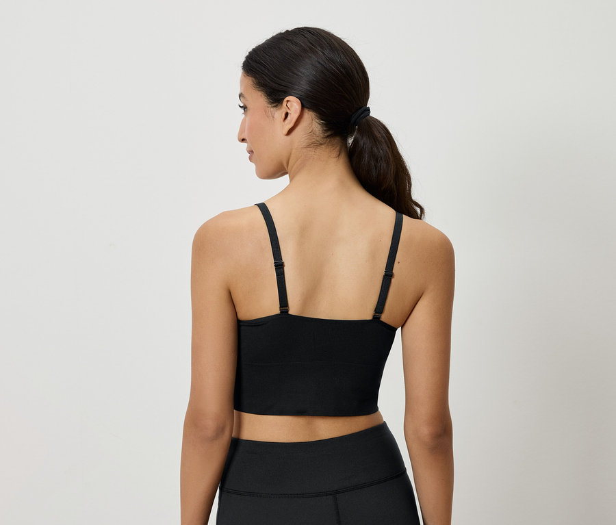 Rückansicht einer Frau mit braunen, zum Pferdeschwanz gebundenen Haaren, die ein schwarzes Sportoberteil und Leggings trägt.