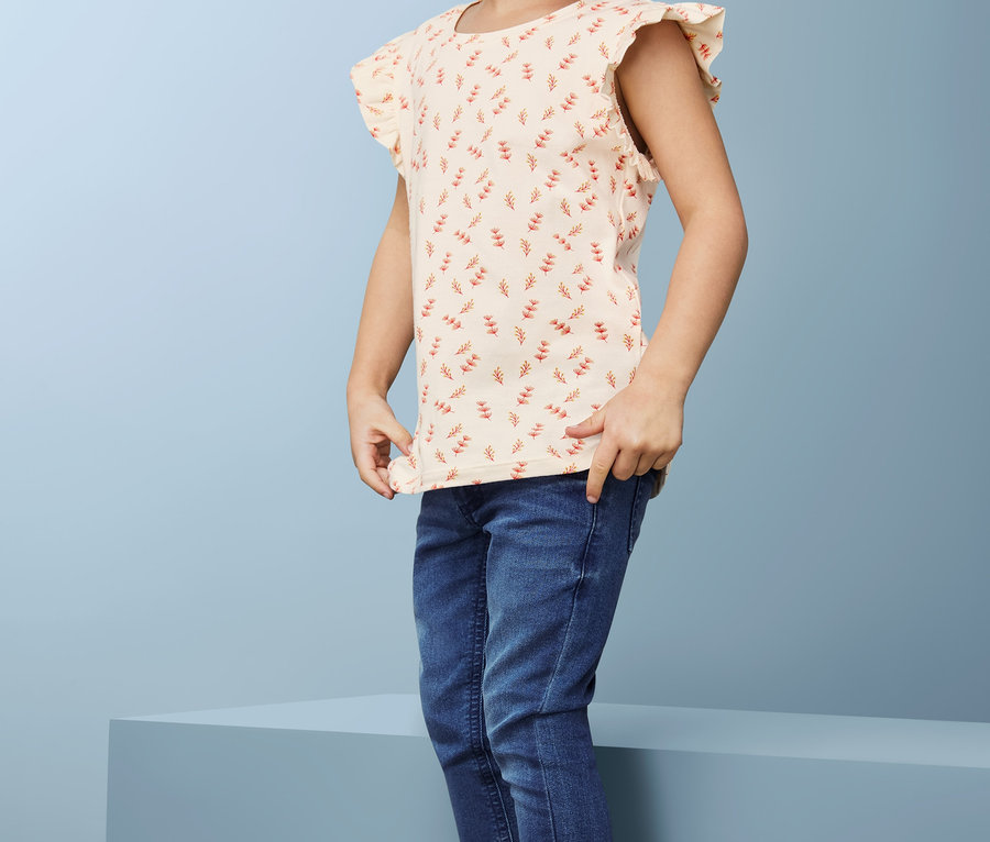 Lächelndes kleines Mädchen, das Jeans und 2 T-Shirts trägt.