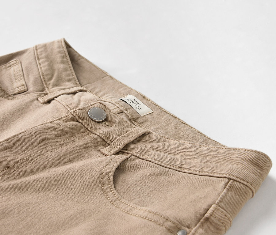 Detailaufnahme einer beigen Hose mit Knopf und Tasche.