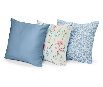Drei Kissen liegen nebeneinander: einfarbig blau, mit Blumenmuster und mit kleinen blauen Blüten auf blauem Grund.