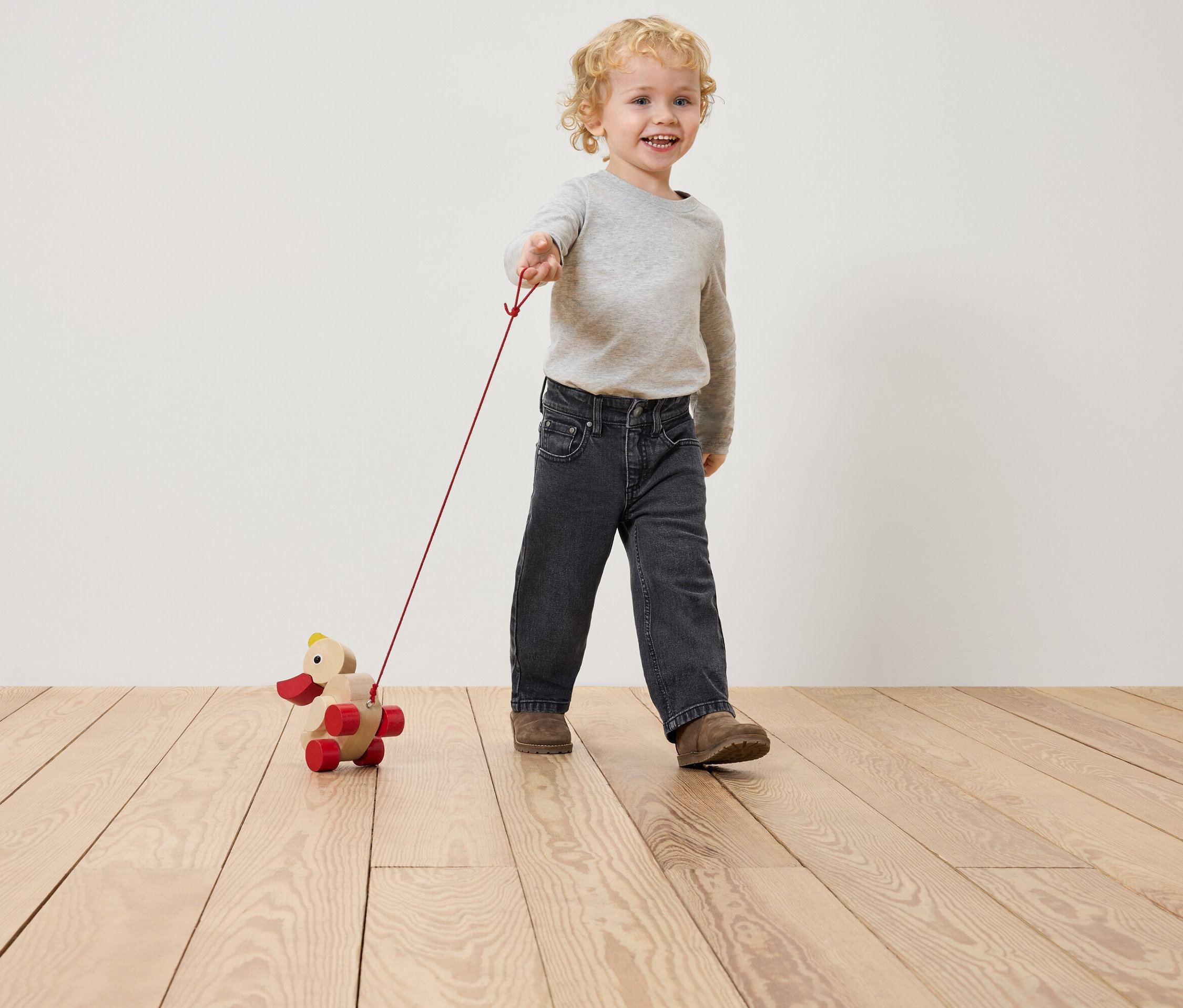 Ein Junge zieht ein hölzernes Entenspielzeug an einer Schnur hinter sich her.