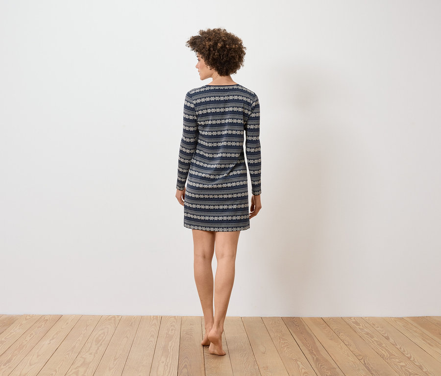 Frau mit lockigem Haar steht mit dem Rücken zum Betrachter und trägt ein blau-weiß gemustertes, langärmeliges Kleid.