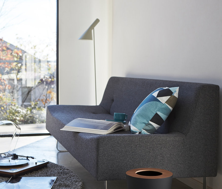 Wohnzimmer mit grauem Sofa, Kissen, Buch, Tasse und schwarzem, runden Yamazaki Mülleimer »RIN«.