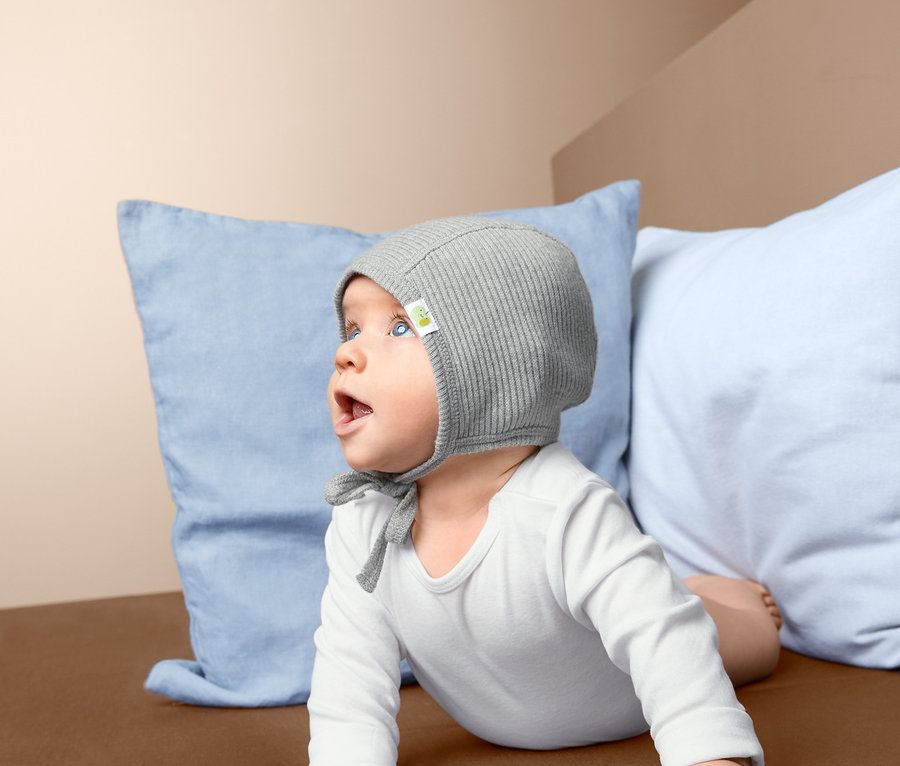 Baby liegt auf dem Bauch auf einer braunen Decke und trägt eine Babymütze.