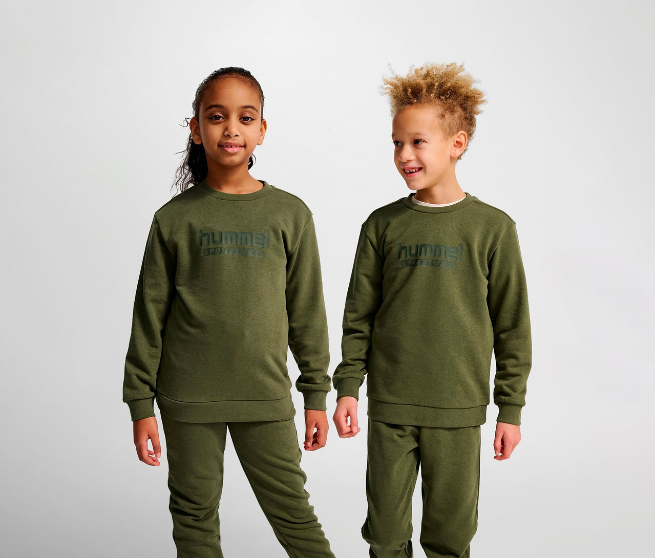 Zwei Kinder stehen nebeneinander und tragen grüne HUMMEL HMLJR Base-Sweatshirts.