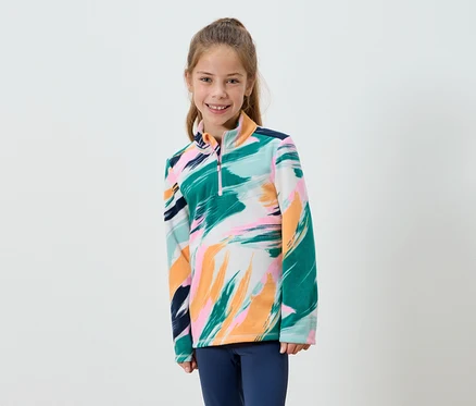 Lächelndes Mädchen trägt ein Fleece mit abstraktem Aufdruck und blaue Hosen.