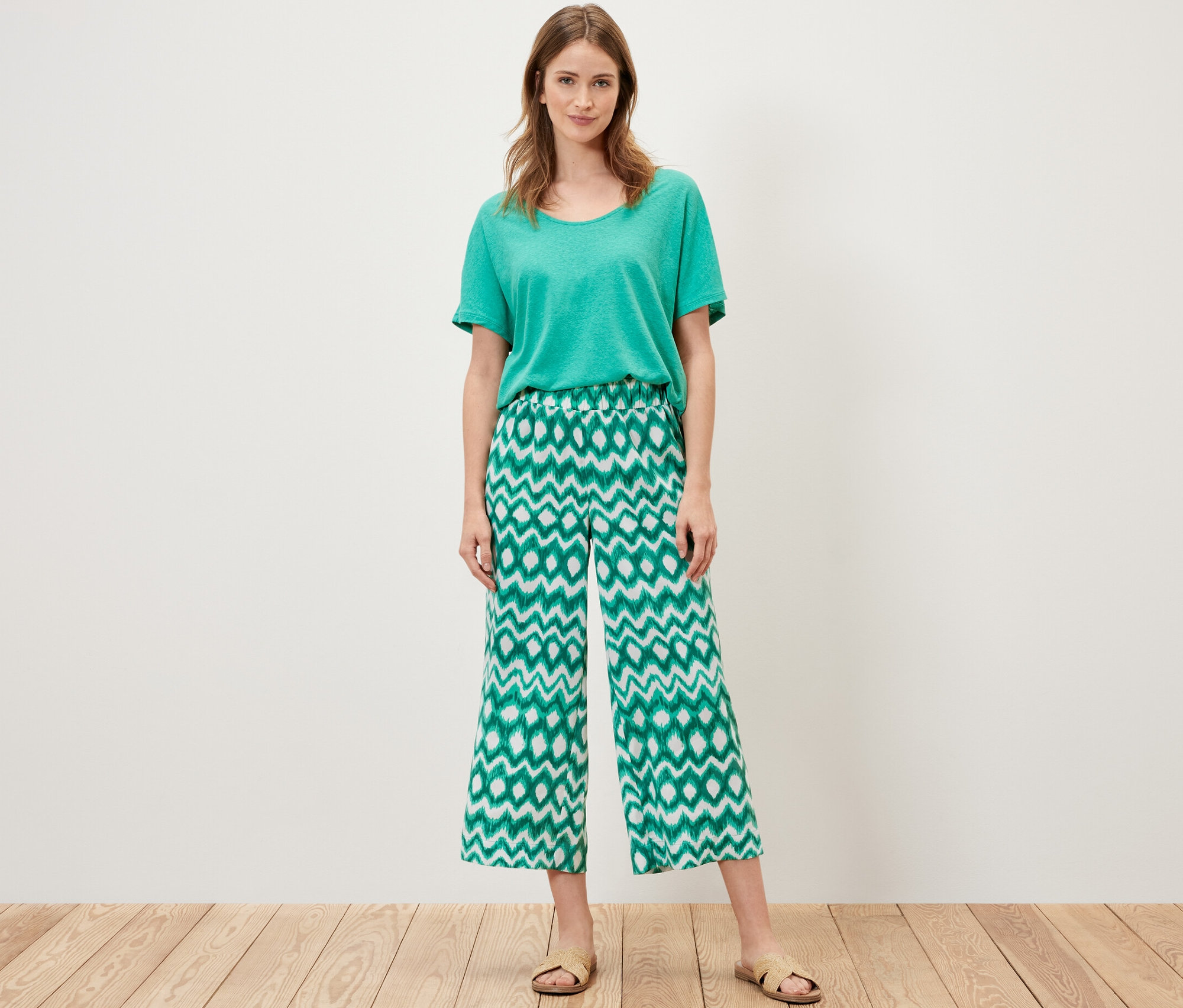 Frau steht und trägt ein grünes T-Shirt und eine bedruckte Satinhose.