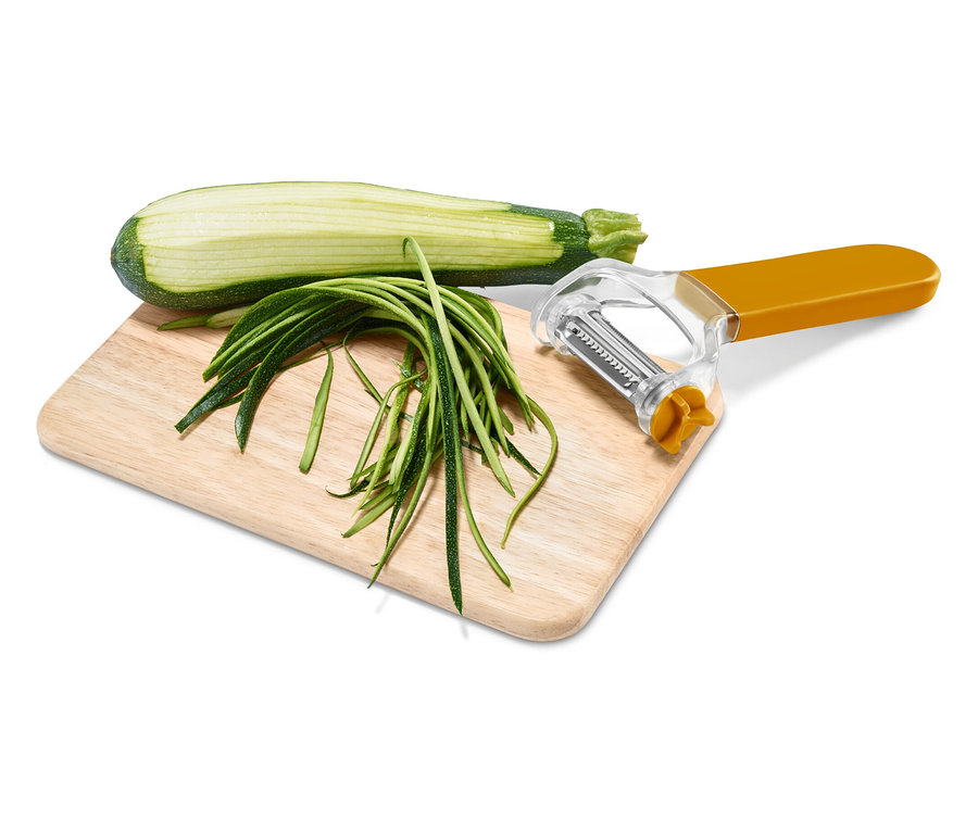 Halbe Zucchini, Zucchinistreifen und ein Schäler mit orangefarbenem Griff auf einem Holzbrett.