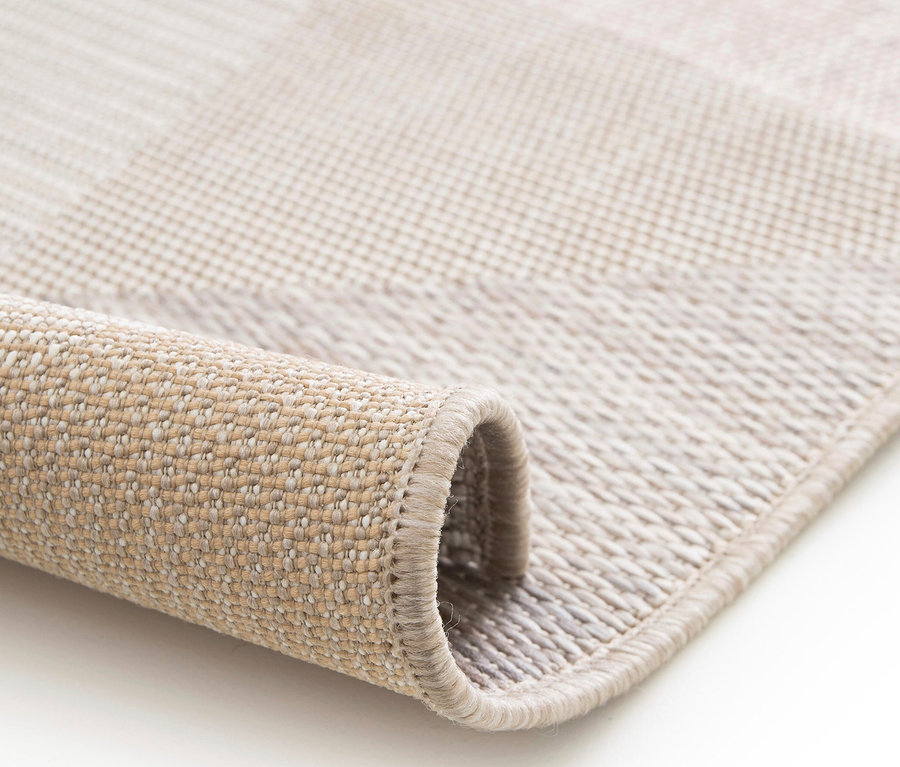 Detailaufnahme eines beigen Outdoor-Teppichs "Sandstone Shapes" mit geometrischem Muster, der teilweise aufgerollt ist.