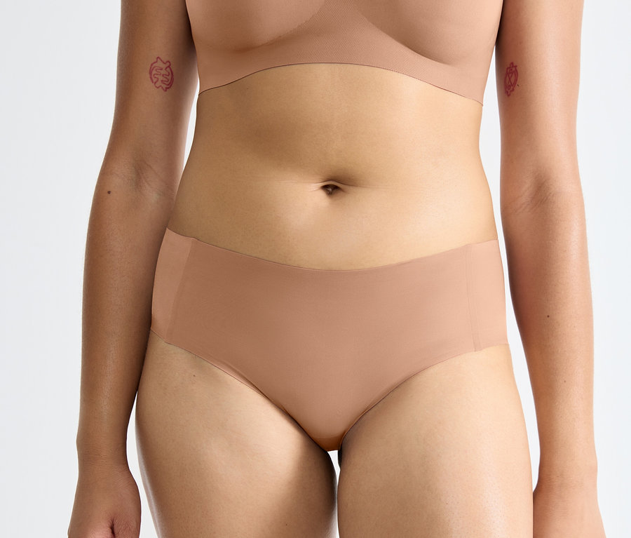 Eine Frau trägt einen braunen, nahtlosen BH und einen Sloggi ZERO Feel 2.0 Hipster in Braun.