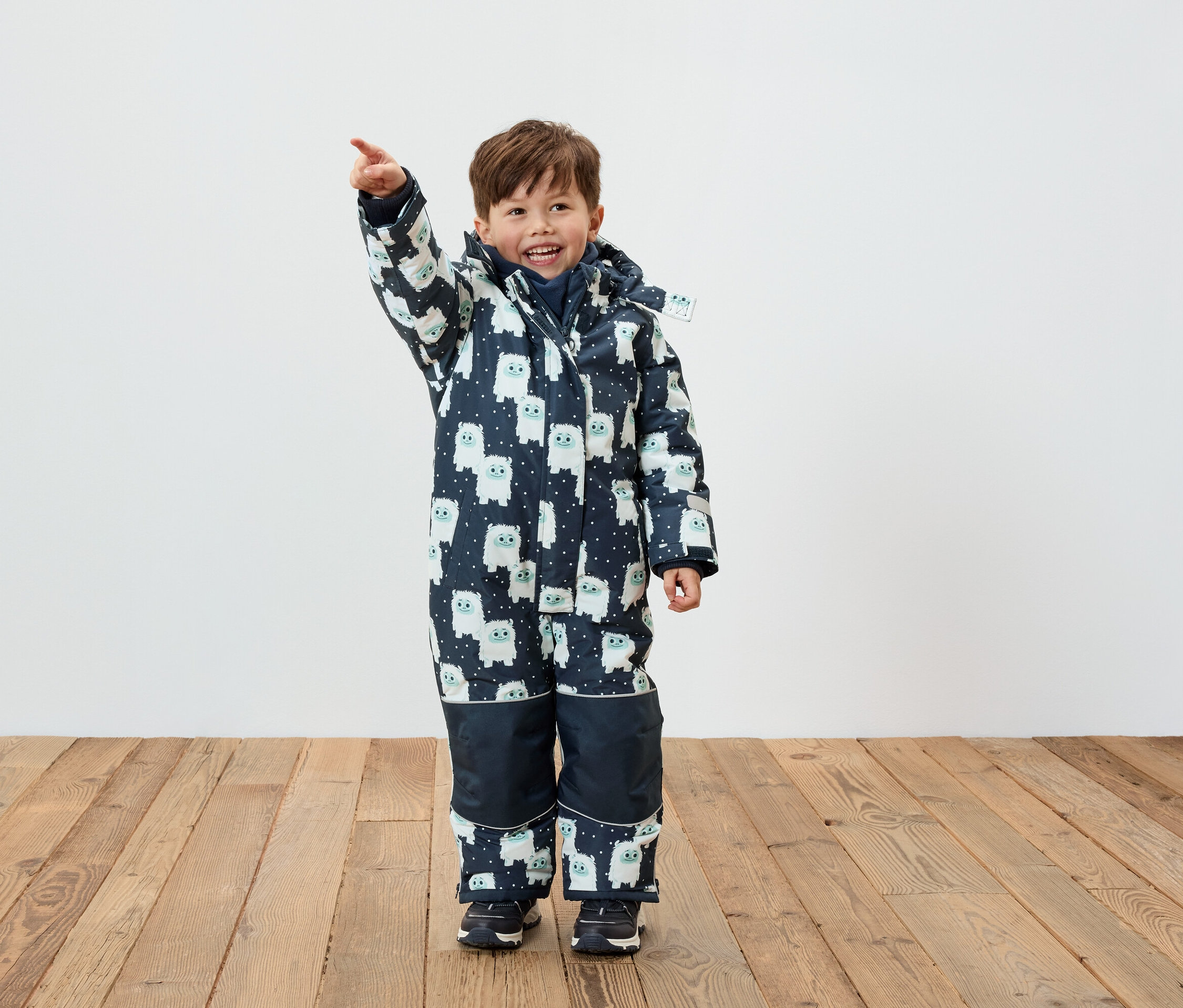 Ein Junge in einem Winteroverall mit Figuren-Muster zeigt mit dem Finger.