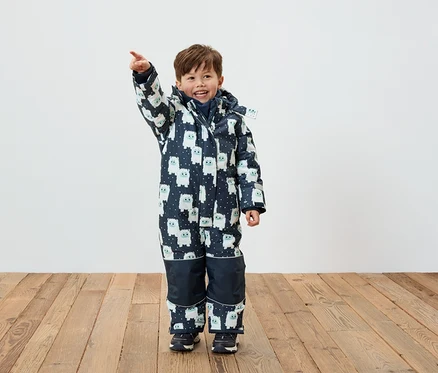 Ein Junge in einem Winteroverall mit Figuren-Muster zeigt mit dem Finger.