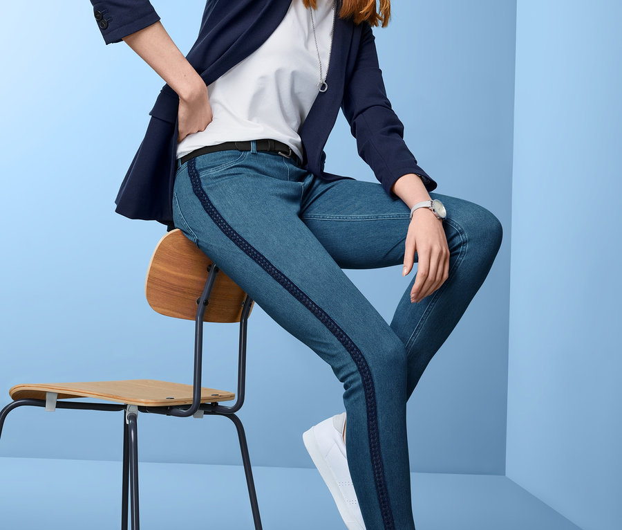 Frau sitzt auf einem Stuhl und trägt Jeggings, Blazer und Turnschuhe.