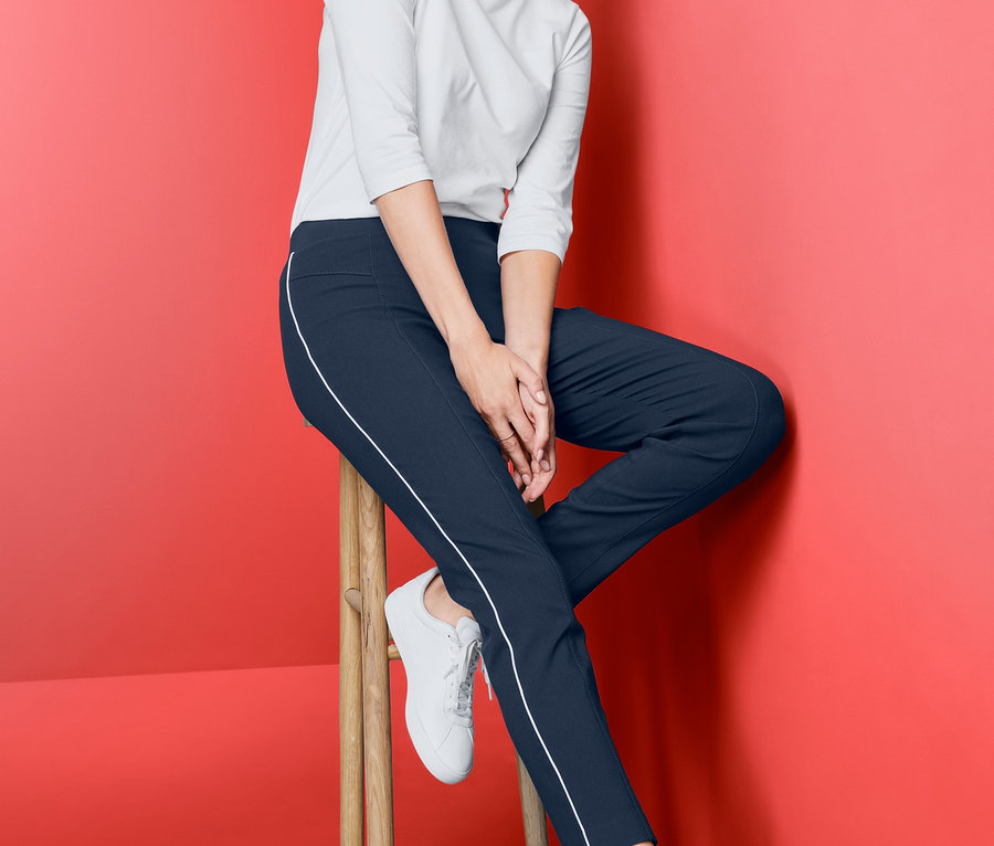 Frau sitzt auf einem Hocker und trägt eine Stretchhose.