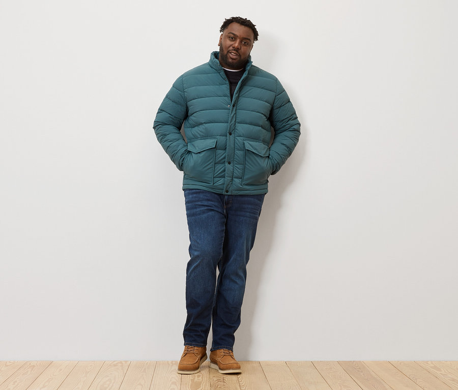 Mann steht mit Steppjacke, Jeans und Schuhen.