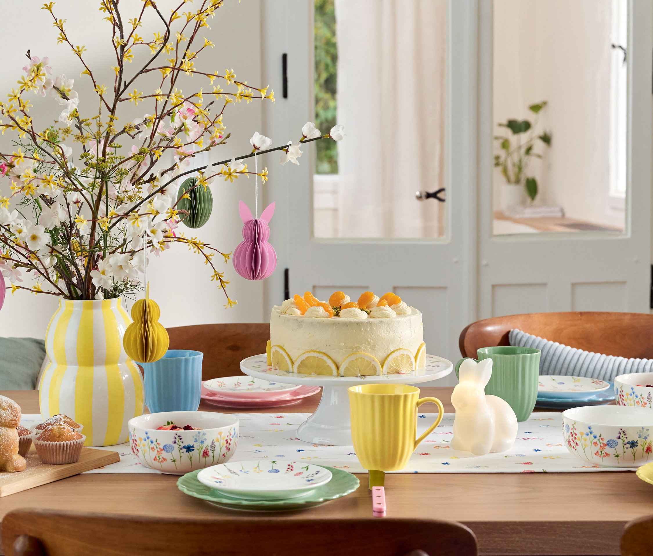 Esstisch mit Osterdekoration, Kuchen, Geschirr und Blumenvase.