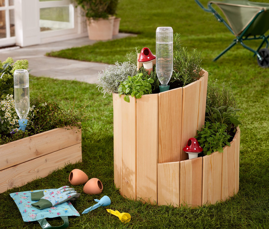 Auf einer Wiese steht ein Hochbeet »Schnecke« aus Holz, bepflanzt mit Kräutern und Gemüse.