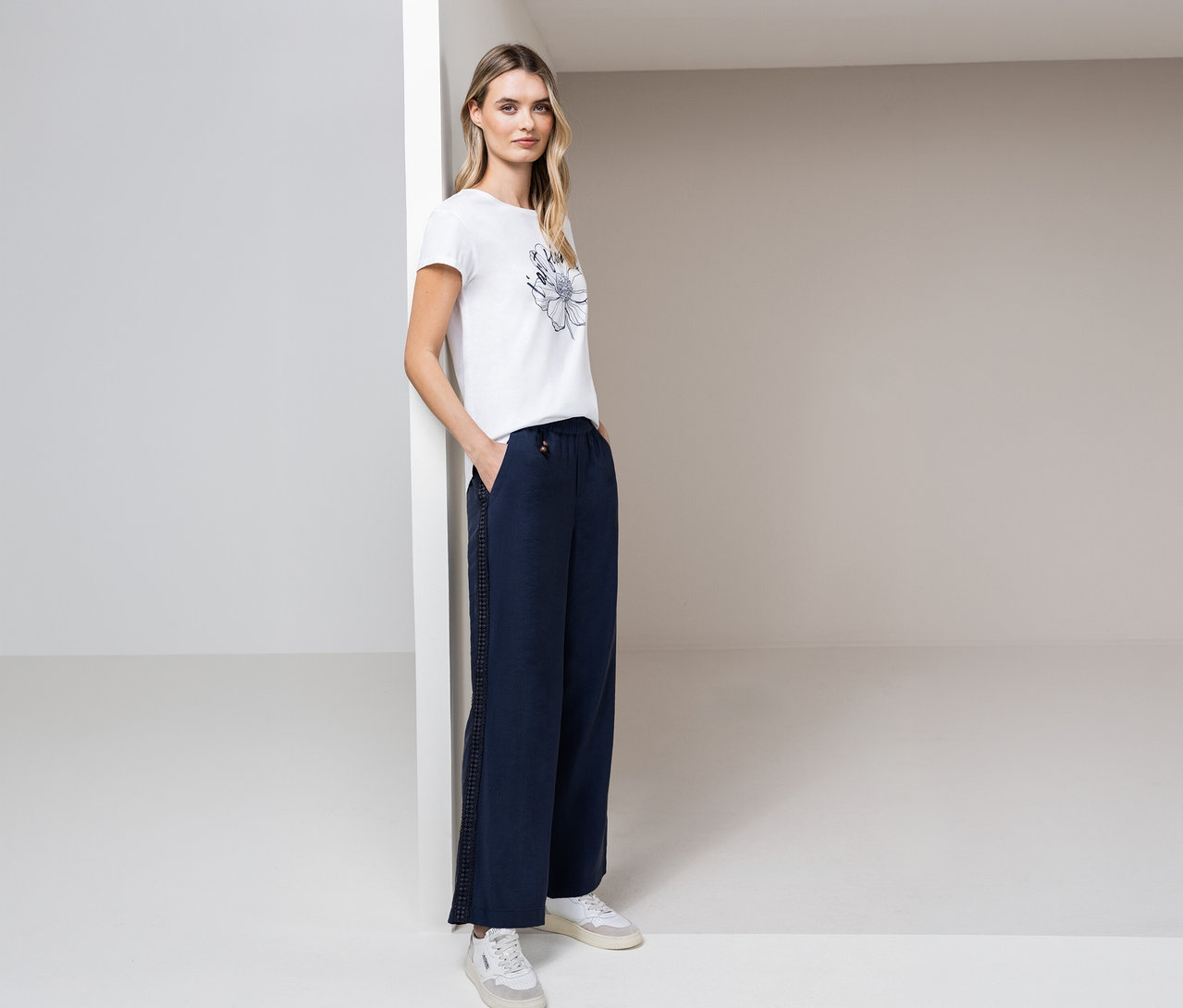 Frau posiert in Street One T-Shirt, blauer Hose und weißen Turnschuhen in einem hellen Raum.