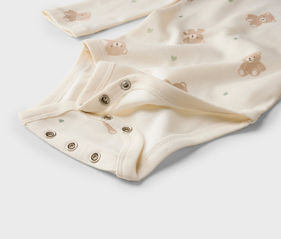 Nahaufnahme eines hellen Baby-Bodys mit Bären- und Herzmuster und Druckknöpfen im Schritt.