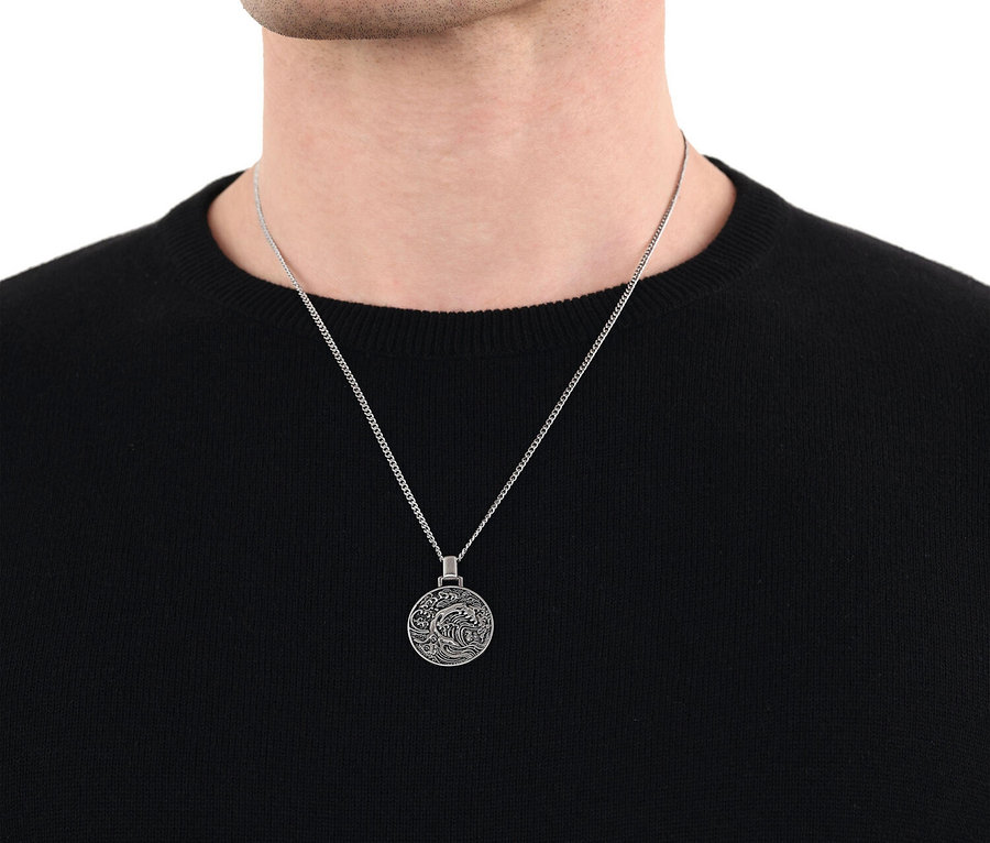Nahaufnahme eines Mannes mit einer silbernen Halskette mit einem runden Anhänger vor einem schwarzen Pullover.