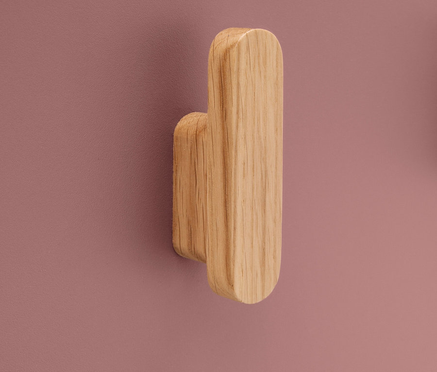 Ein hölzerner Wandhaken ist an einer rosafarbenen Wand befestigt.
