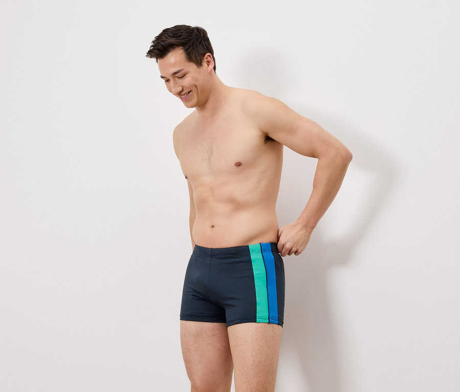 Mann trägt dunkelblaue Badehose mit grünen und blauen Streifen.