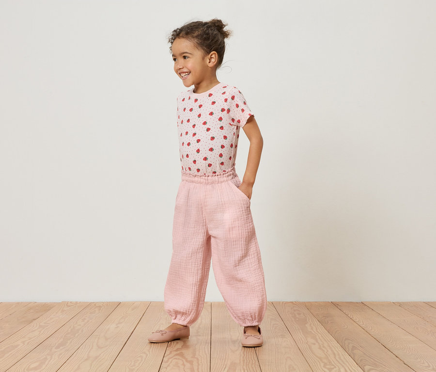 Ein junges Mädchen steht auf einem Holzboden und trägt ein rosa Erdbeer-T-Shirt und eine rosafarbene Hose.