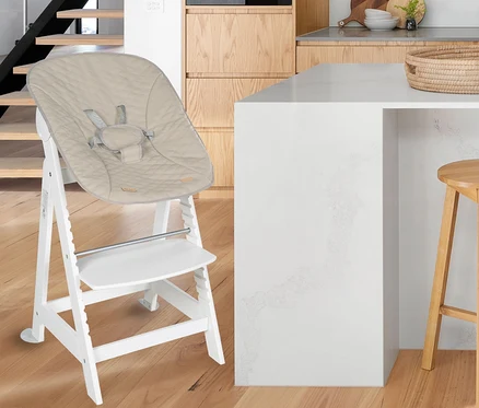 Ein weißer Kinderhochstuhl mit einem beigen Sitzkissen steht auf einem Holzboden.