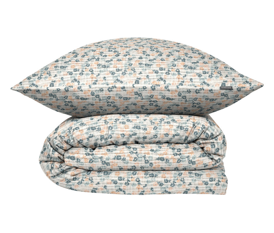 Ein Kissen liegt auf einer gefalteten Bettdecke mit einem Blumenmuster.