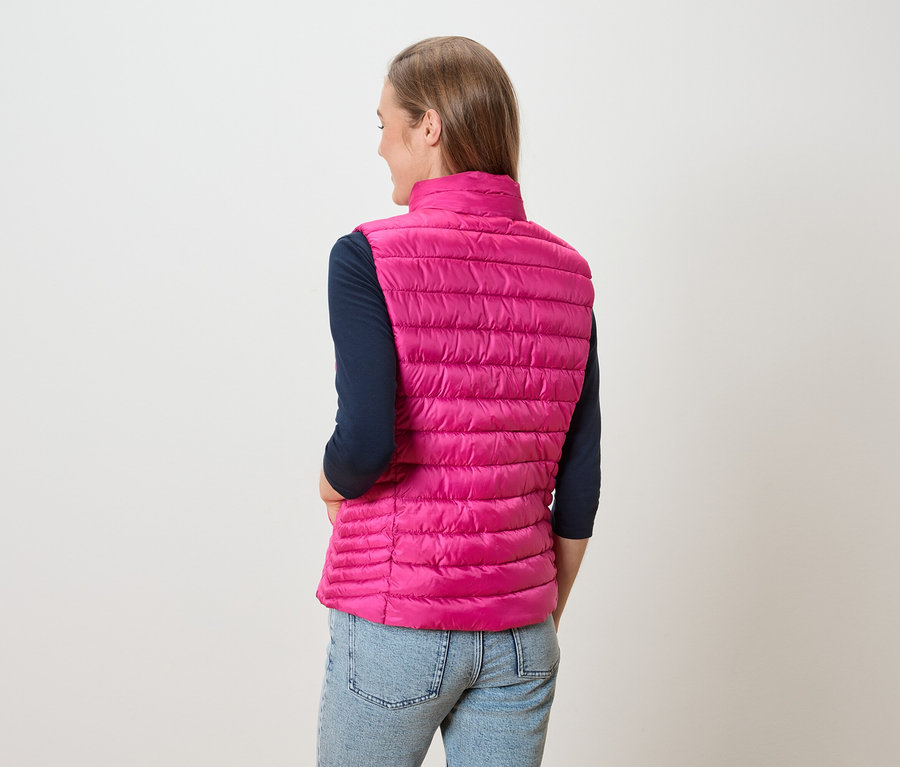 Frau von hinten, trägt eine pinke Steppweste über einem marineblauen Langarmshirt und Jeans.