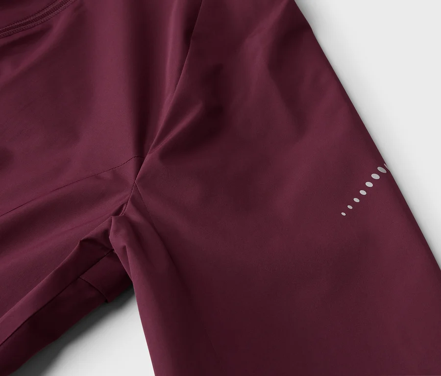 Nahaufnahme einer weinroten Jacke mit Reißverschluss und reflektierenden Punkten am Ärmel.