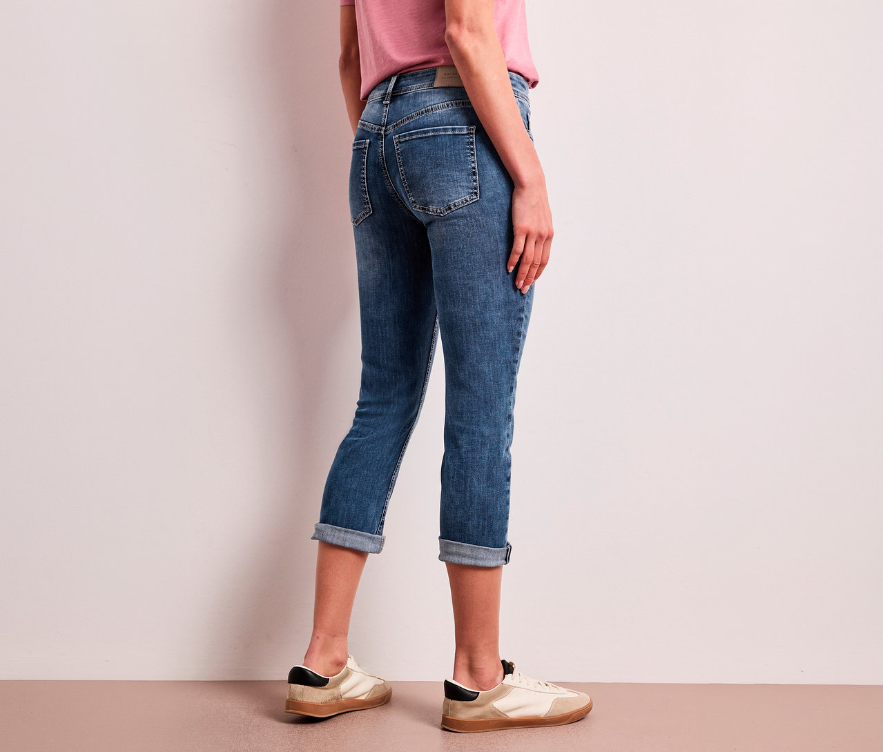 Eine Person von hinten, die blaue, hochgekrempelte Street One 7/8-Jeans »Jane« und helle Sneaker trägt.