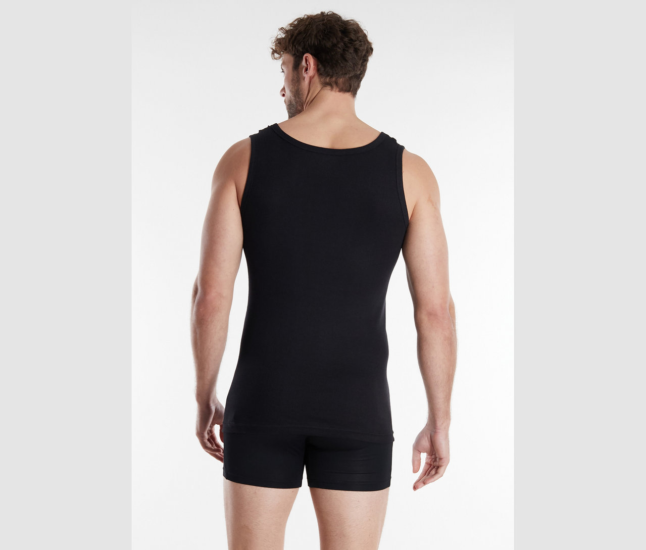 Mann von hinten in schwarzem Unterhemd und Shorts vor weißem Hintergrund.