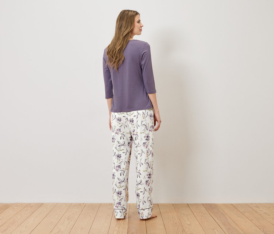 Frau steht mit dem Rücken zur Kamera und trägt ein lila Pyjamaoberteil und eine weiße Pyjamahose mit Blumenmuster.