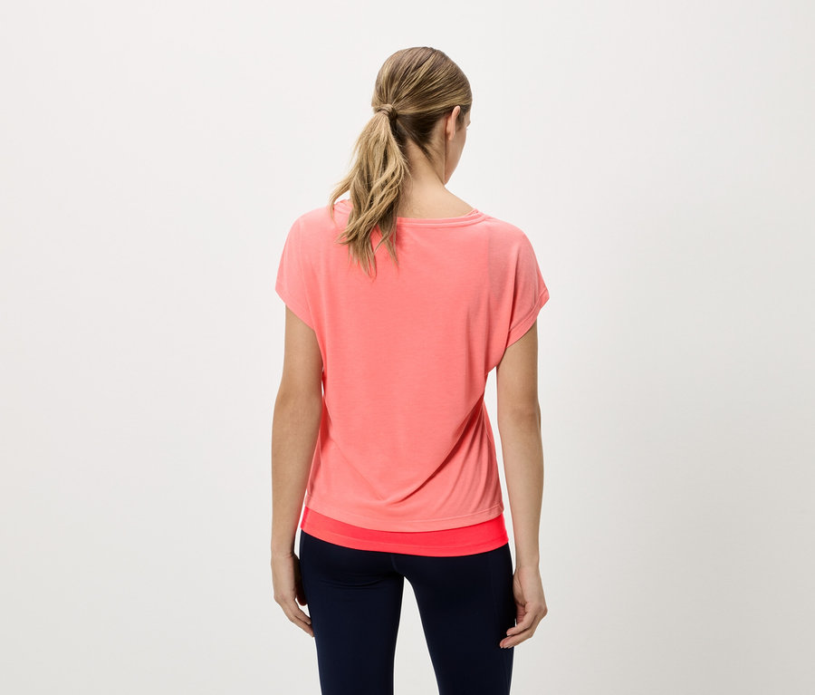 Rückansicht einer Frau mit blondem Haar, die ein korallfarbenes T-Shirt und marineblaue Leggings trägt.