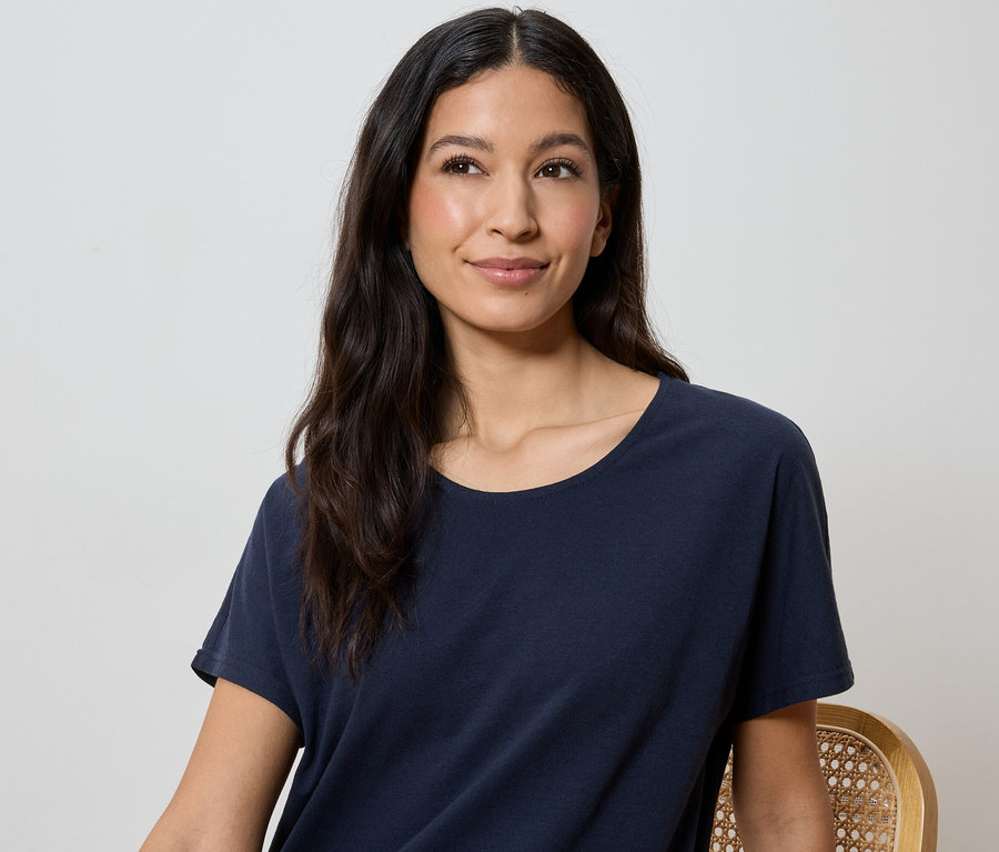 Frau mit langen, dunklen Haaren trägt ein marineblaues T-Shirt.