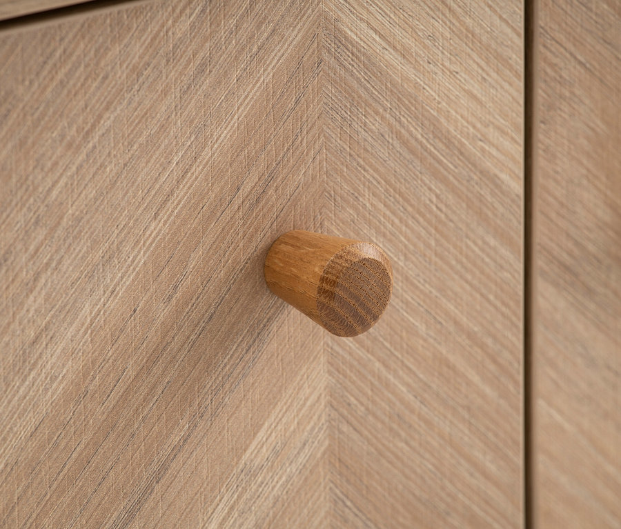 Detailaufnahme eines hellbraunen Holzschranks mit einem runden Holzgriff.