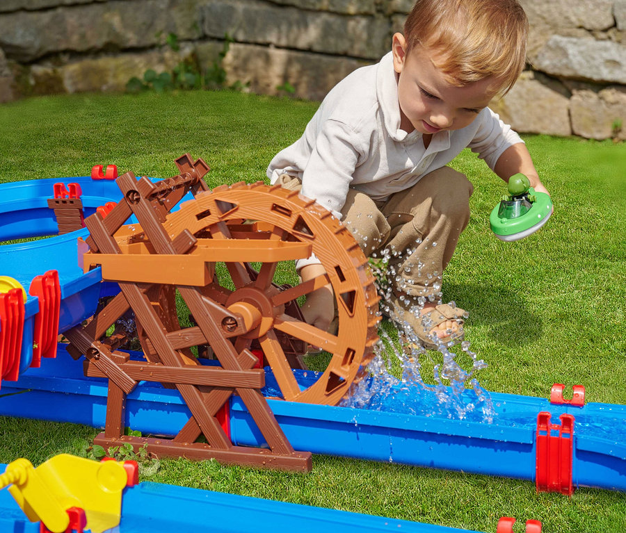 Junge spielt mit AquaPlay Wasserbahn »WaterWheel« auf Rasen, hält Boot mit Figur über Wasserrad.