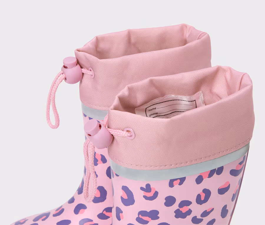 Nahaufnahme von rosa Gummistiefeln mit lila Leopardenmuster und Namensschild.