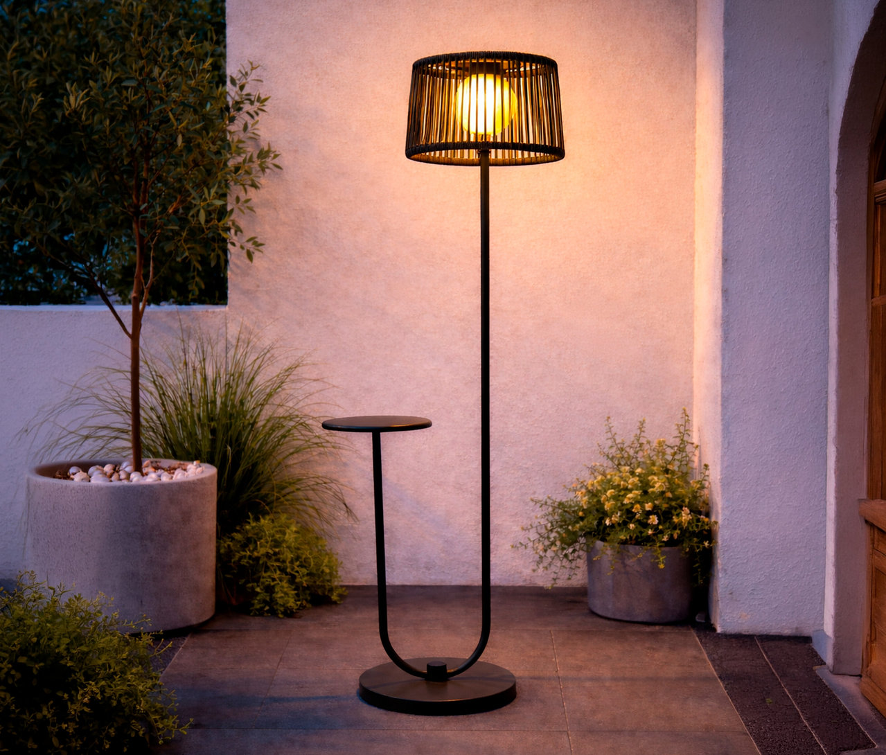 Eine anthrazitfarbene Leco Solar Stehleuchte mit integriertem Tisch steht auf einer Terrasse neben Pflanzen.