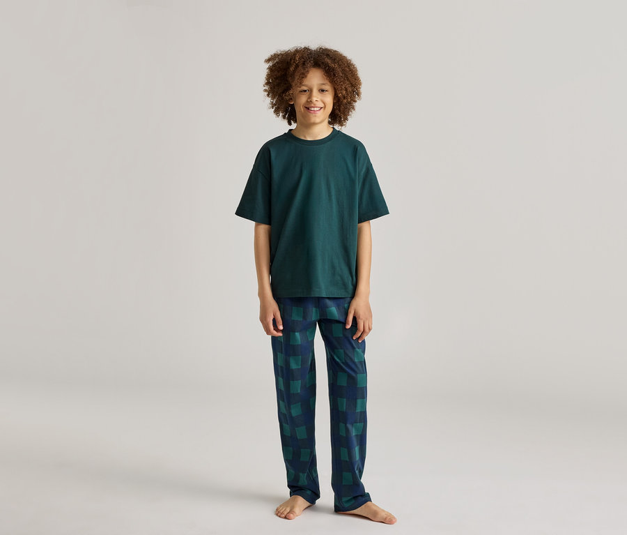Ein lächelnder Junge mit lockigem Haar trägt einen dunkelgrünen Pyjama mit karierter Hose.