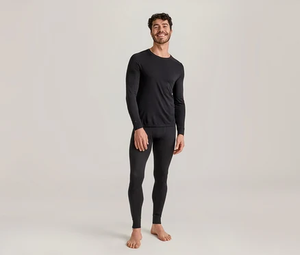 Lächelnder Mann in schwarzem, langärmeligem Thermoshirt und schwarzer Thermoleggings, barfuß stehend.