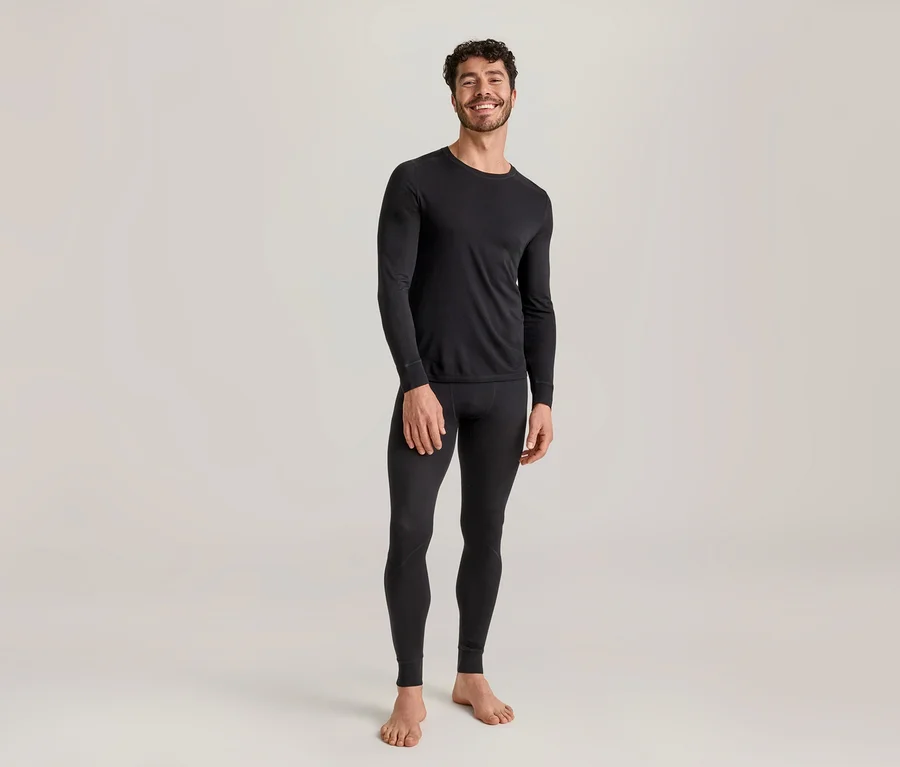 Lächelnder Mann in schwarzem, langärmeligem Thermoshirt und schwarzer Thermoleggings, barfuß stehend.