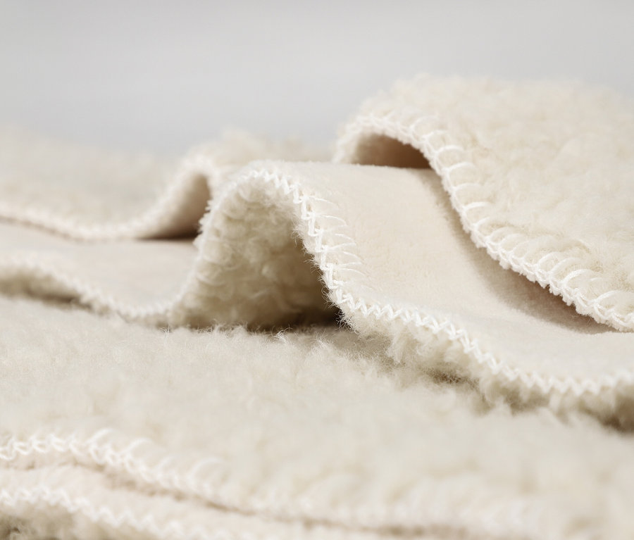 Nahaufnahme eines cremefarbenen, flauschigen Stoffes oder einer Decke, gefaltet, um die weiche Textur und die weiß genähten Kanten zu zeigen.