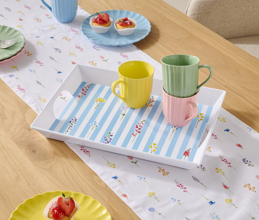 Esstisch mit Geschirr und Tassen auf einer floralen Tischdecke.