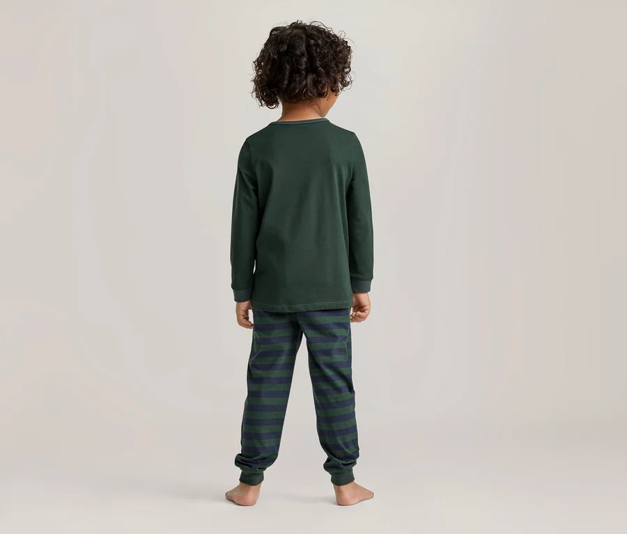 Kind von hinten gesehen, trägt ein dunkelgrünes Langarmshirt und dunkelgrün-marineblaue gestreifte Pyjamahosen. Barfuß mit lockigem dunklem Haar.