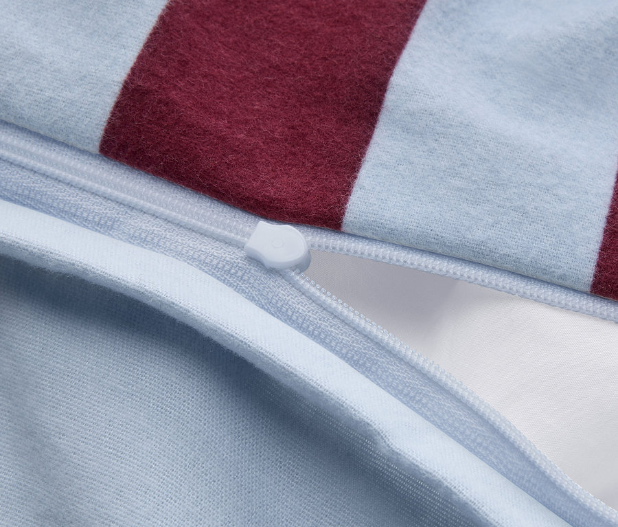Nahaufnahme eines hellblauen und bordeauxroten gestreiften Stoffes mit einem teilweise geöffneten hellblauen Reißverschluss, der weißen Stoff im Inneren zeigt.