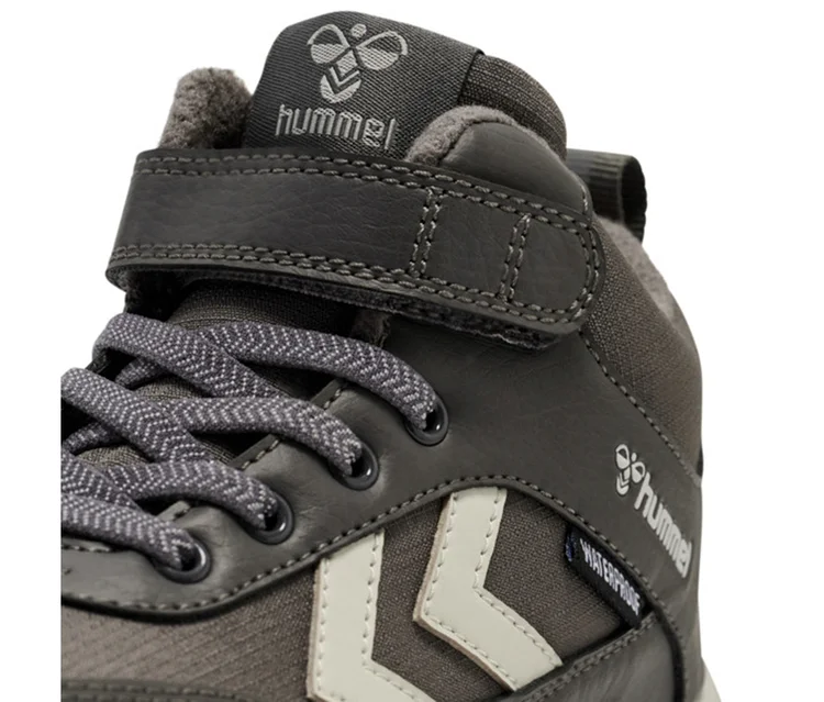 Nahaufnahme eines dunkelgrauen hummel® Turnschuhs »Root Tex Jr« mit hellgrauen Akzenten, Schnürsenkeln, Klettverschluss und „WATERPROOF“-Schriftzug.
