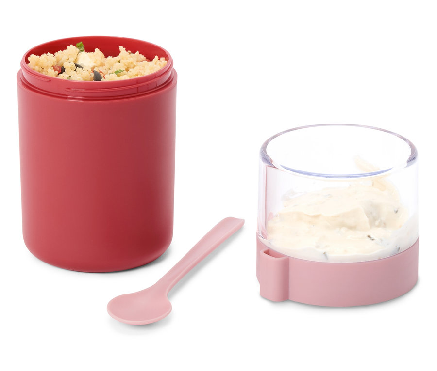 Offener roter Lebensmittelbehälter mit Getreidesalat, daneben ein kleinerer rosa-transparenter Behälter mit cremigem Dip und ein rosa Löffel auf weißem Hintergrund.